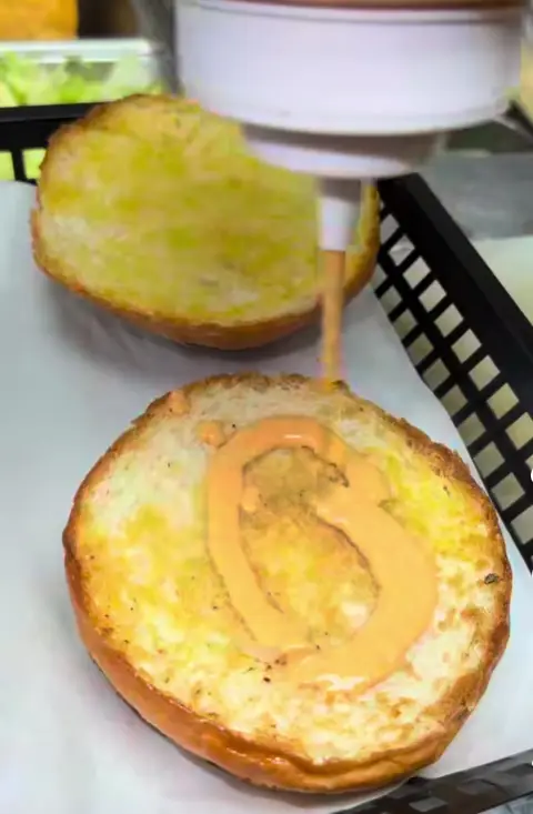 Sauce being spread on a toasted burger bun